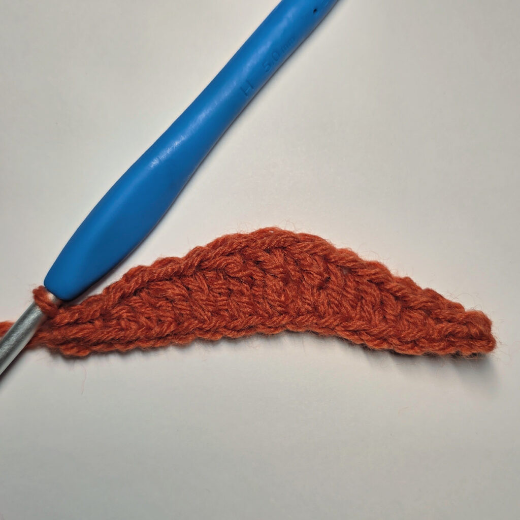 Working an orange crochet pumpkin with a blue crochet hook.