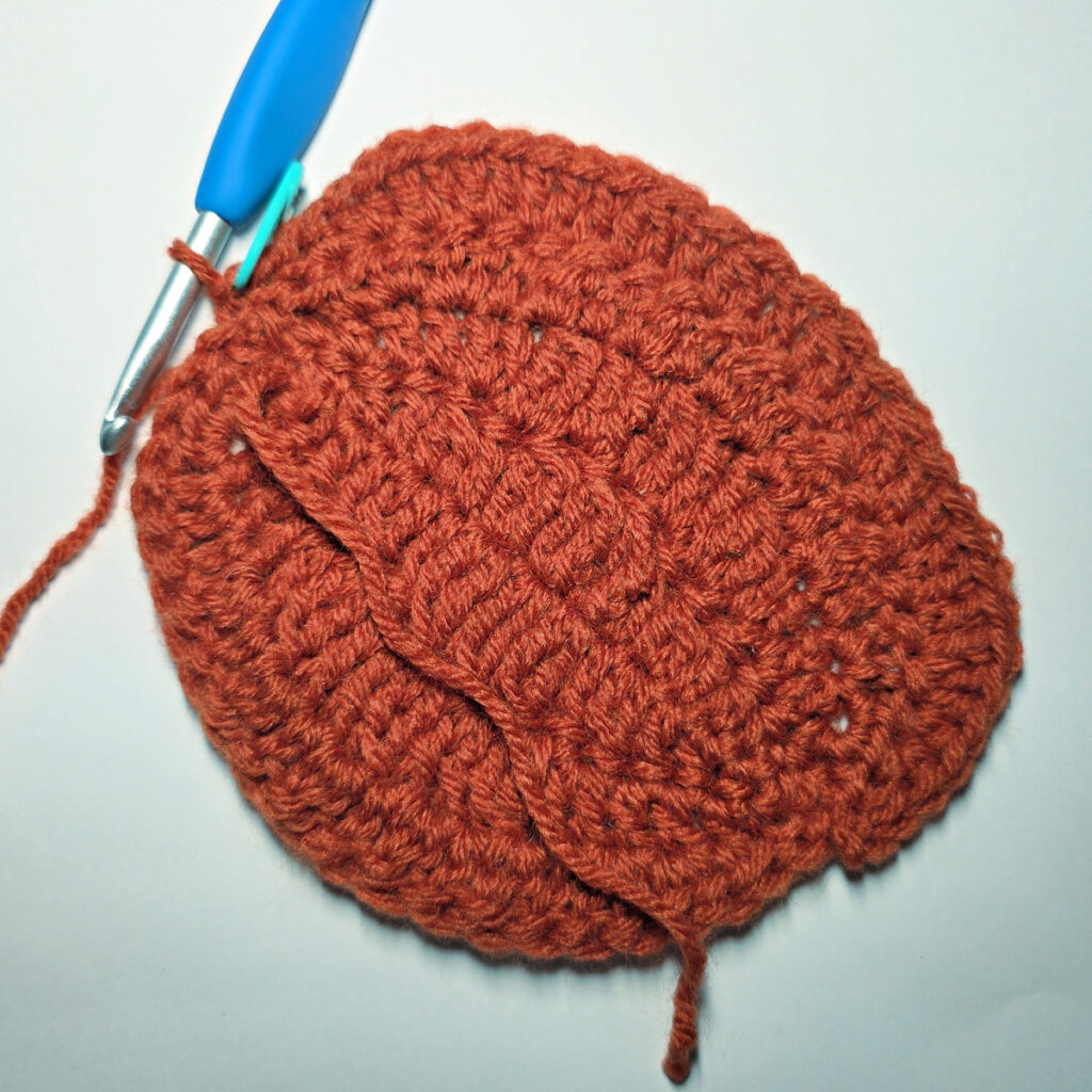 Working an orange crochet pumpkin with a blue crochet hook.