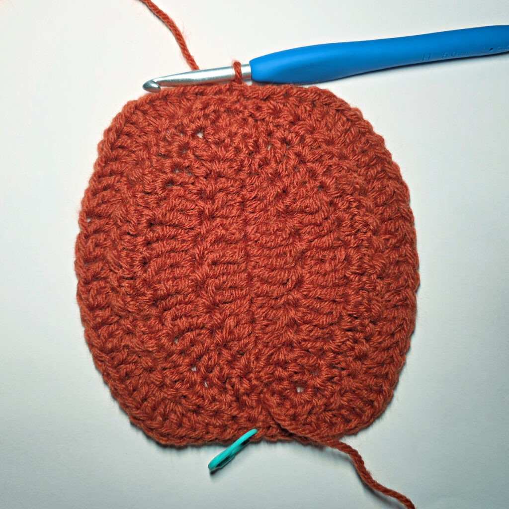 Working an orange crochet pumpkin with a blue crochet hook.