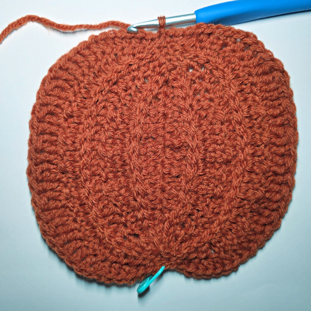 Working an orange crochet pumpkin with a blue crochet hook.