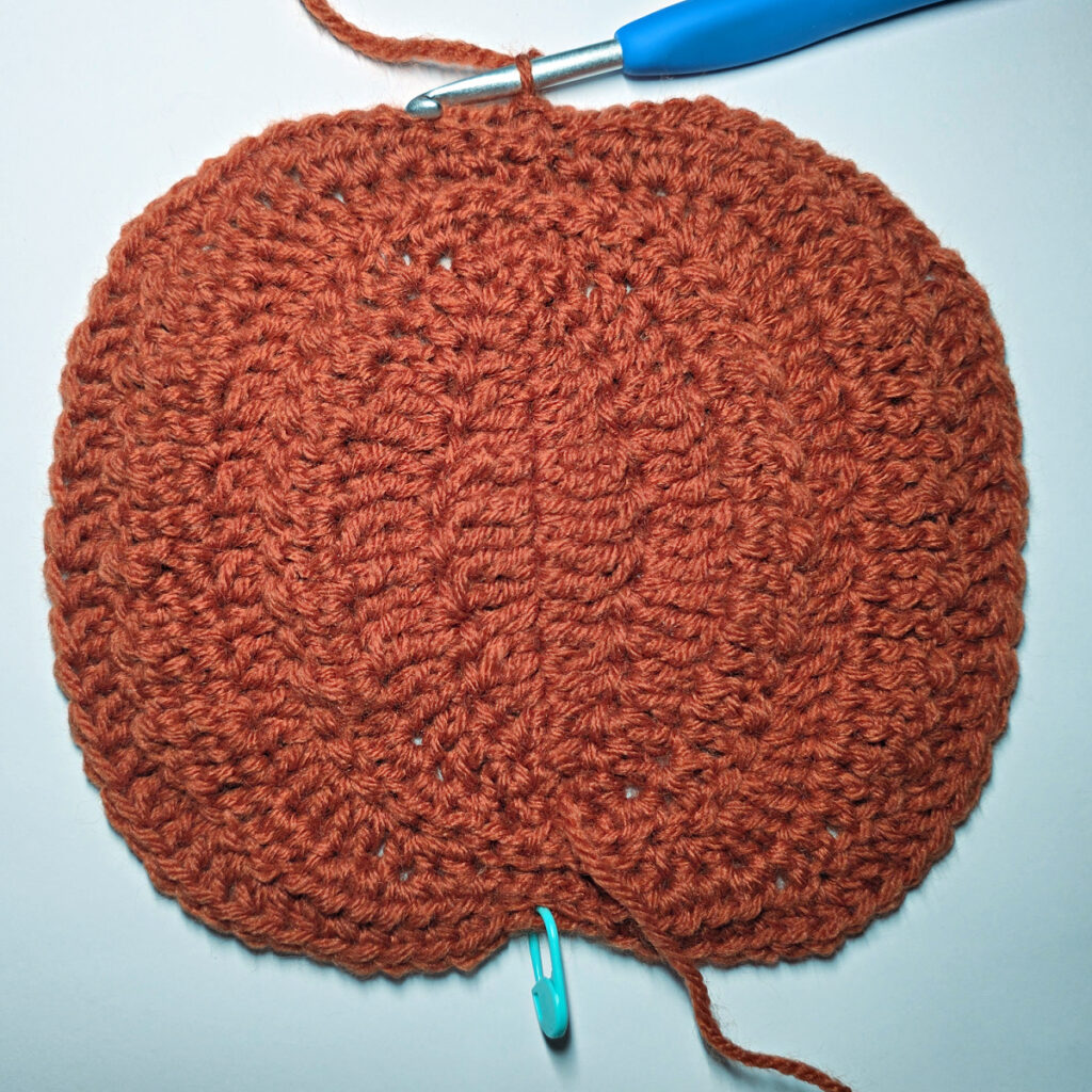 Working an orange crochet pumpkin with a blue crochet hook.