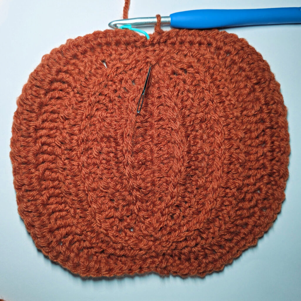 Working an orange crochet pumpkin with a blue crochet hook.