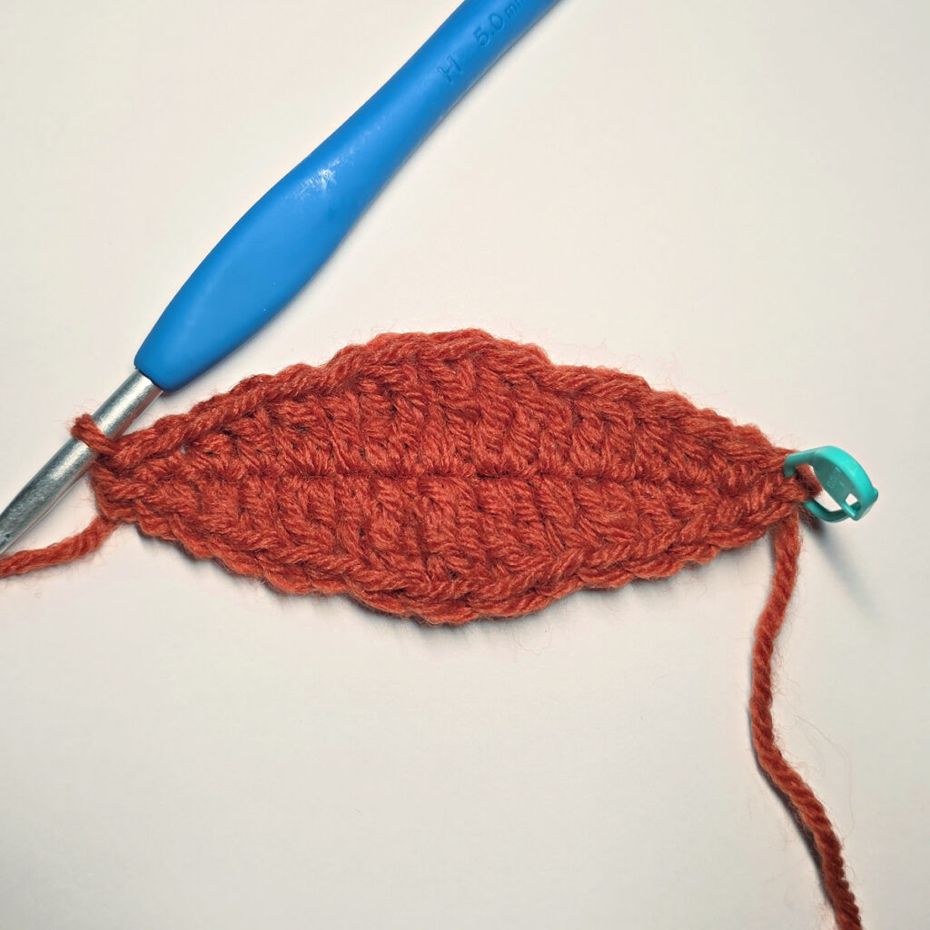 Working an orange crochet pumpkin with a blue crochet hook.
