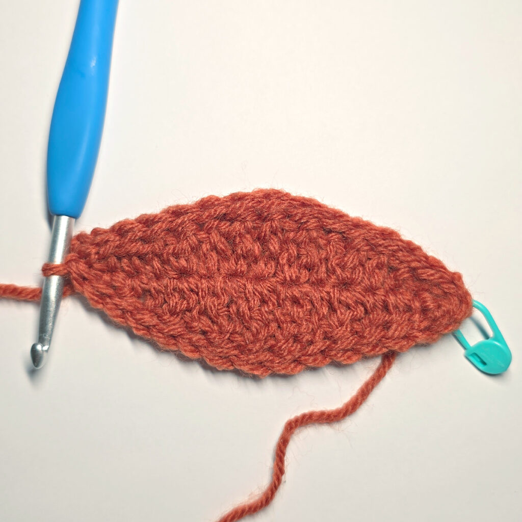 Working an orange crochet pumpkin with a blue crochet hook.