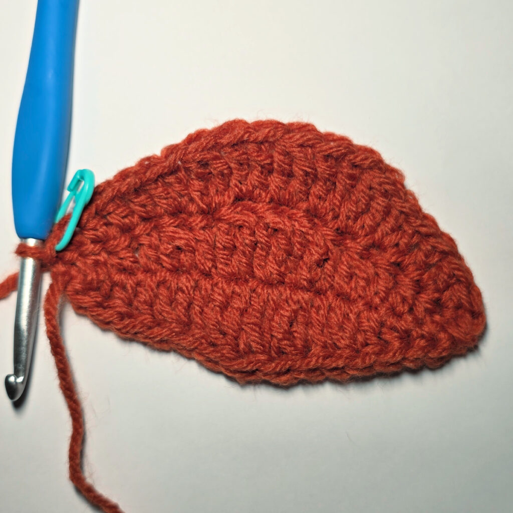 Working an orange crochet pumpkin with a blue crochet hook.