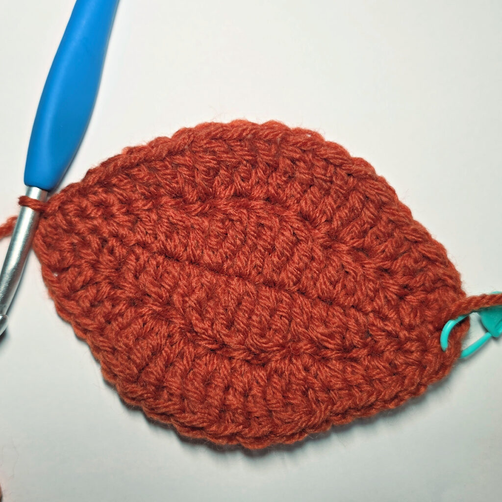 Working an orange crochet pumpkin with a blue crochet hook.