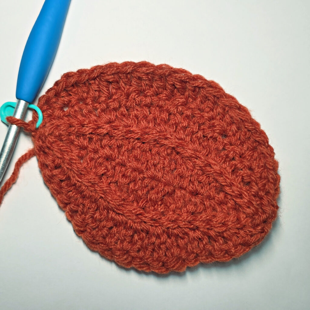 Working an orange crochet pumpkin with a blue crochet hook.