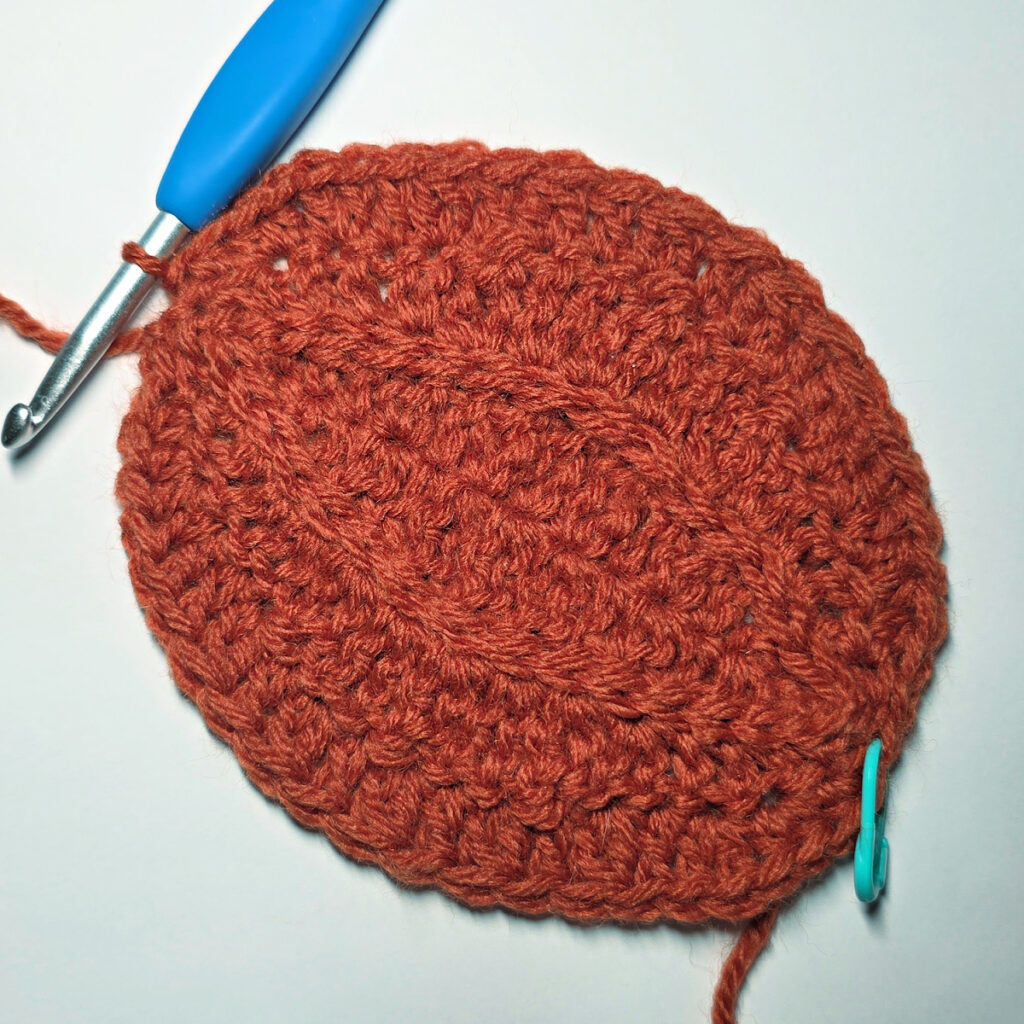 Working an orange crochet pumpkin with a blue crochet hook.