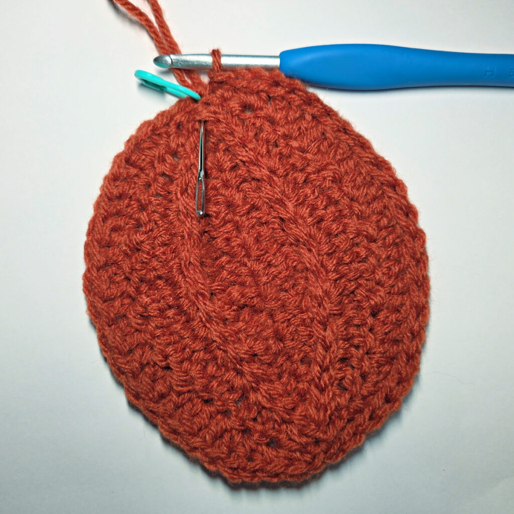 Working an orange crochet pumpkin with a blue crochet hook.