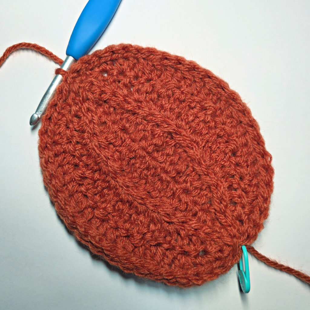 Working an orange crochet pumpkin with a blue crochet hook.