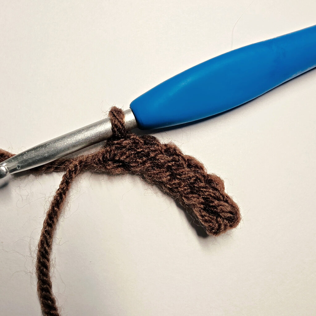 Making a brown crochet pumpkin stem with a blue crochet hook.