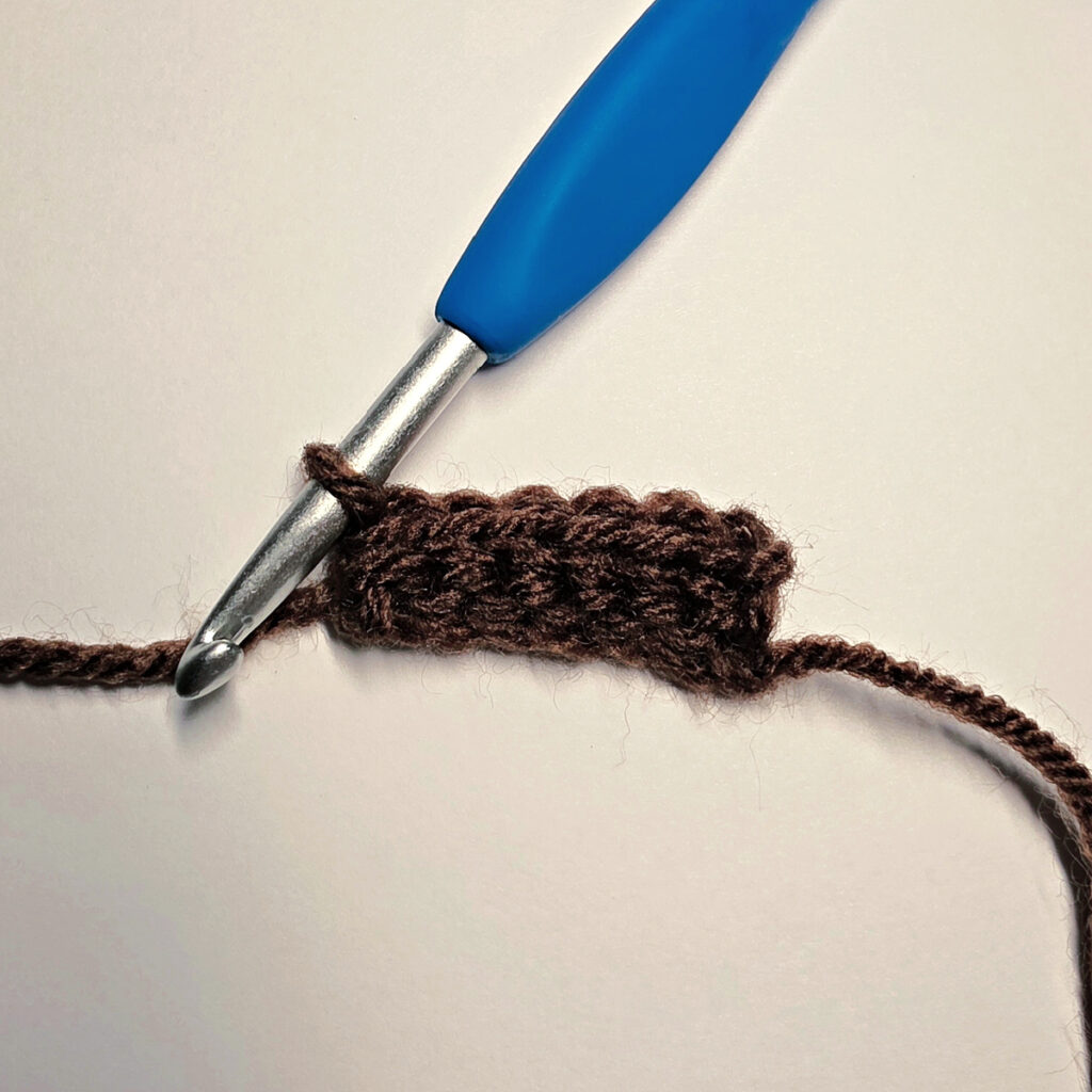 Making a brown crochet pumpkin stem with a blue crochet hook.
