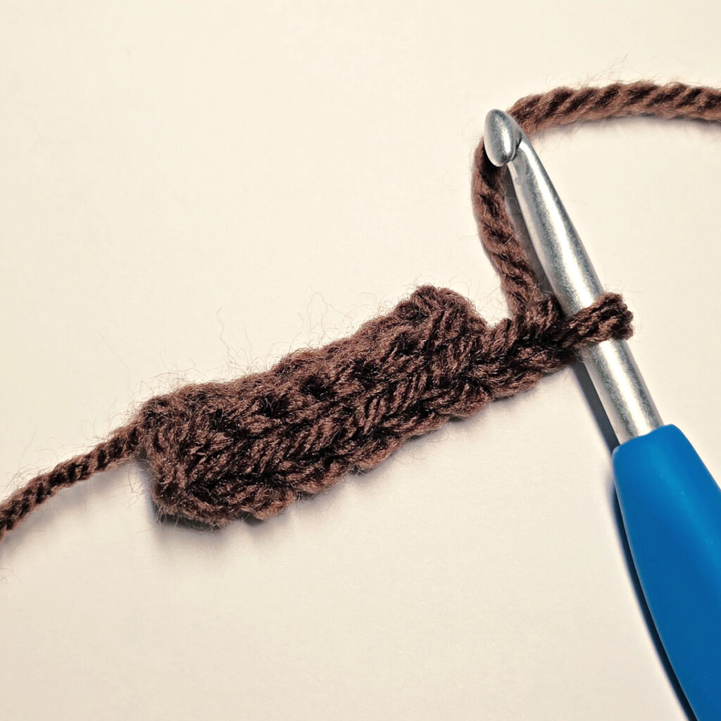 Making a brown crochet pumpkin stem with a blue crochet hook.