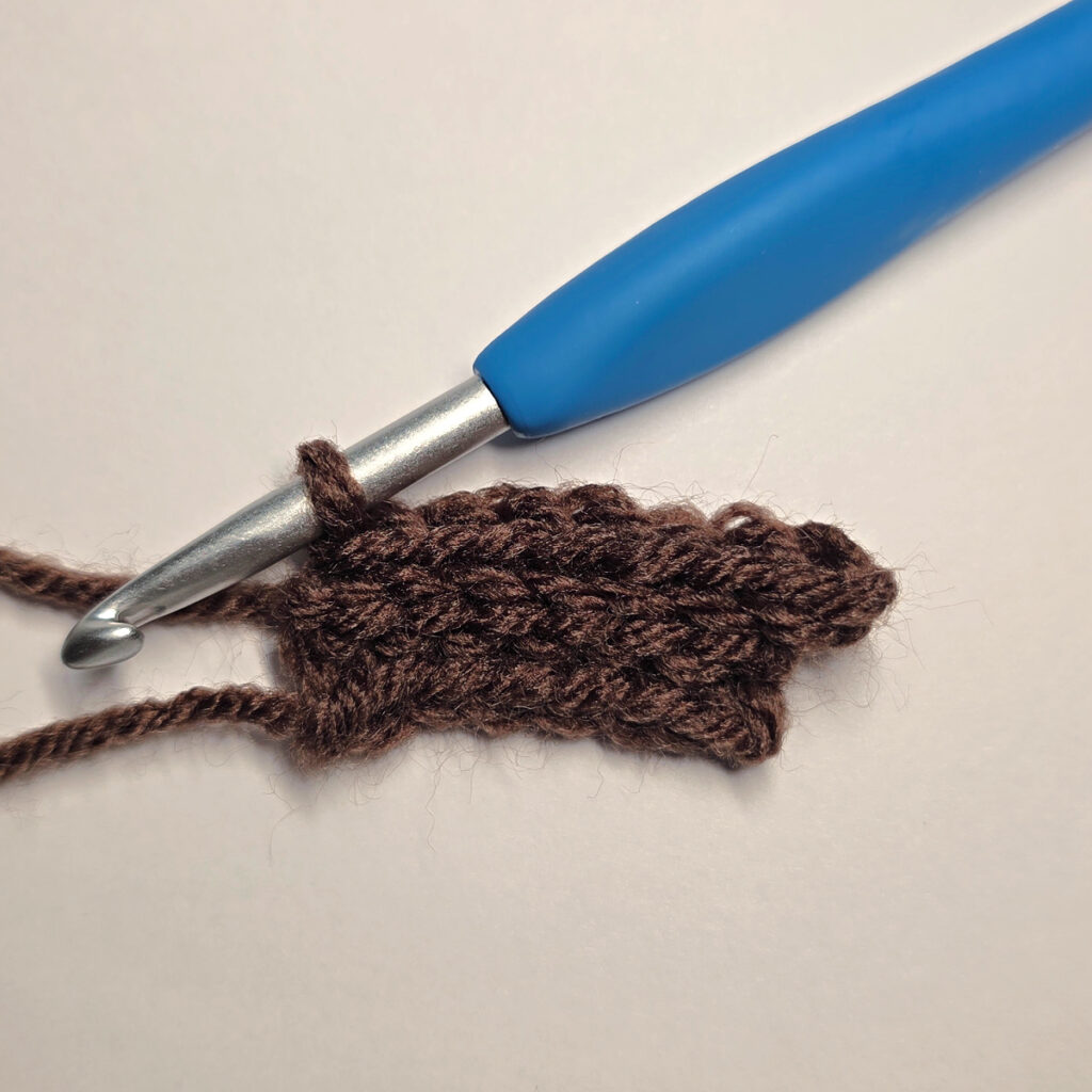Making a brown crochet pumpkin stem with a blue crochet hook.