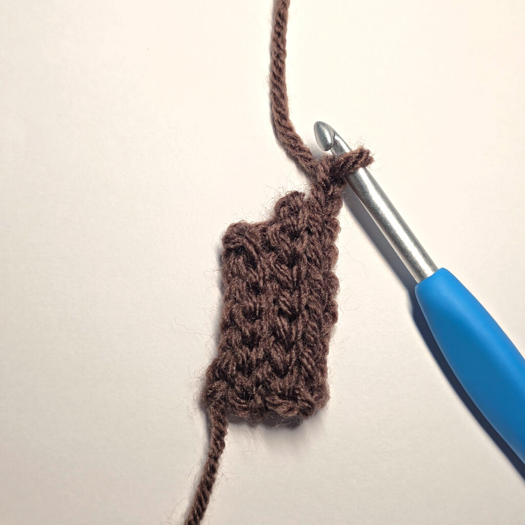Making a brown crochet pumpkin stem with a blue crochet hook.