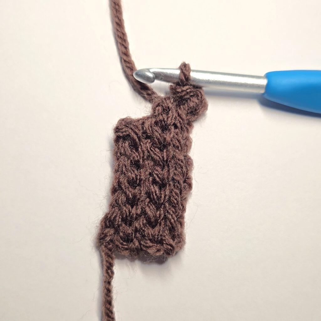 Making a brown crochet pumpkin stem with a blue crochet hook.