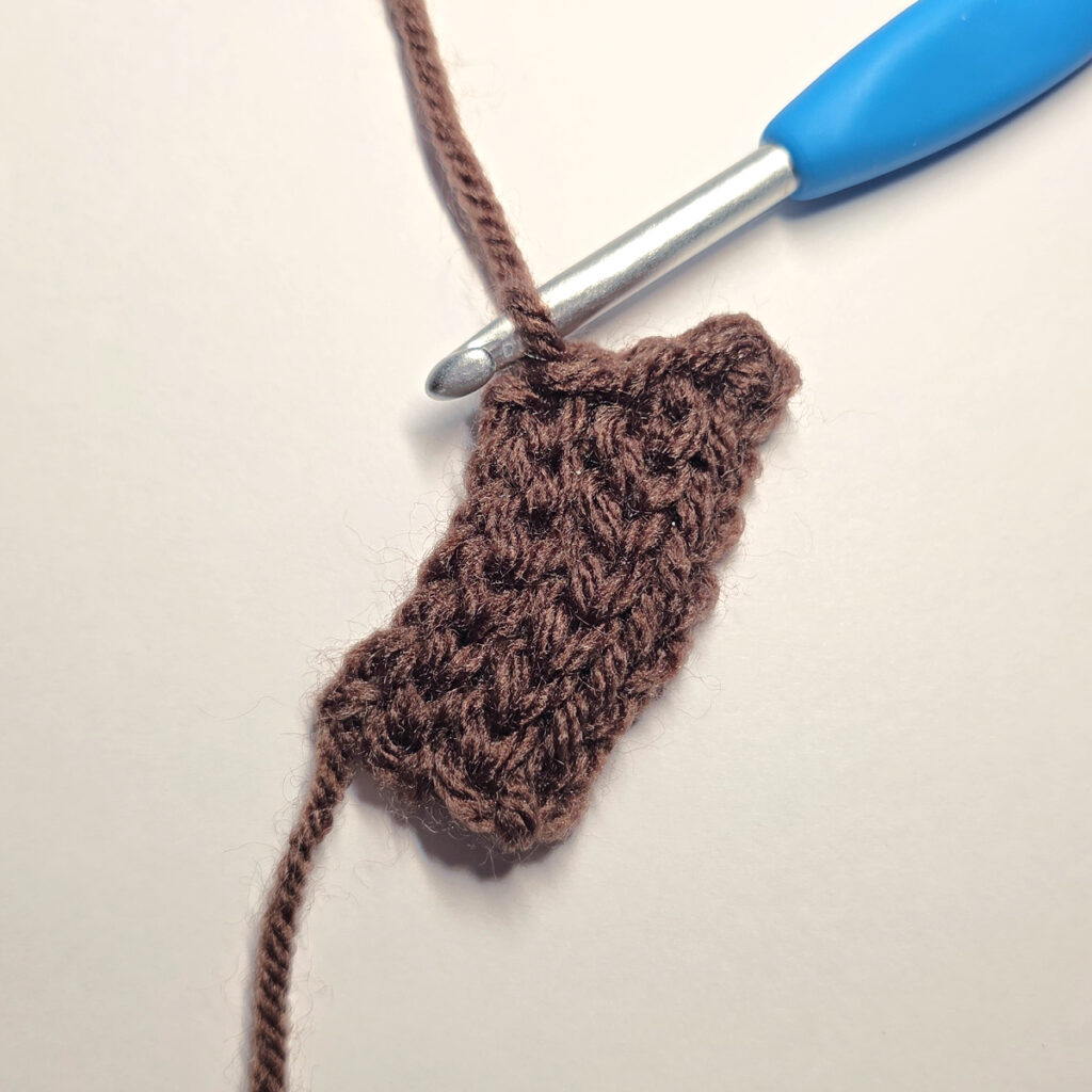 Making a brown crochet pumpkin stem with a blue crochet hook.
