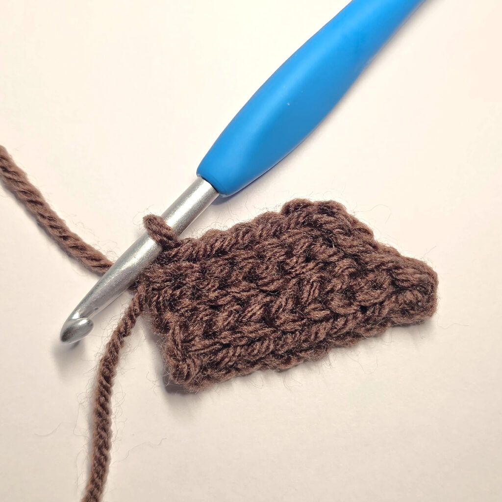 Making a brown crochet pumpkin stem with a blue crochet hook.