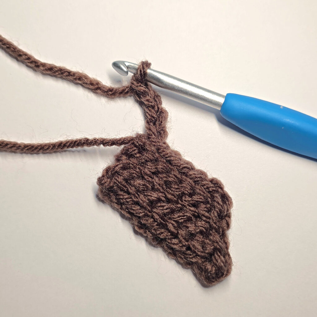 Making a brown crochet pumpkin stem with a blue crochet hook.