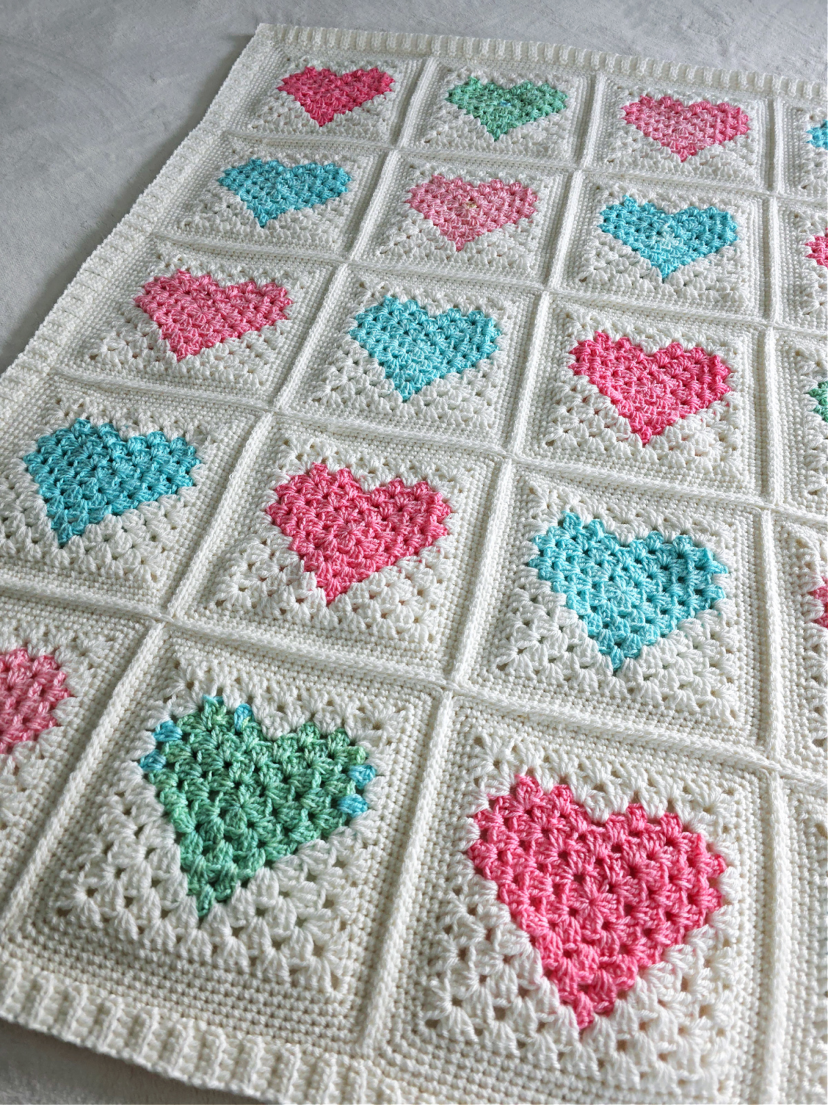 White crochet quilt made from pink and blue heart motifs spread out.