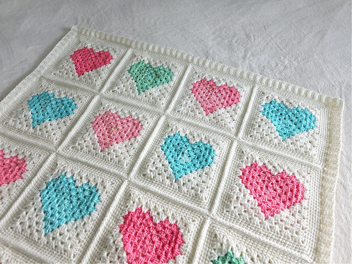 White crochet quilt made from pink and blue heart motifs spread out.