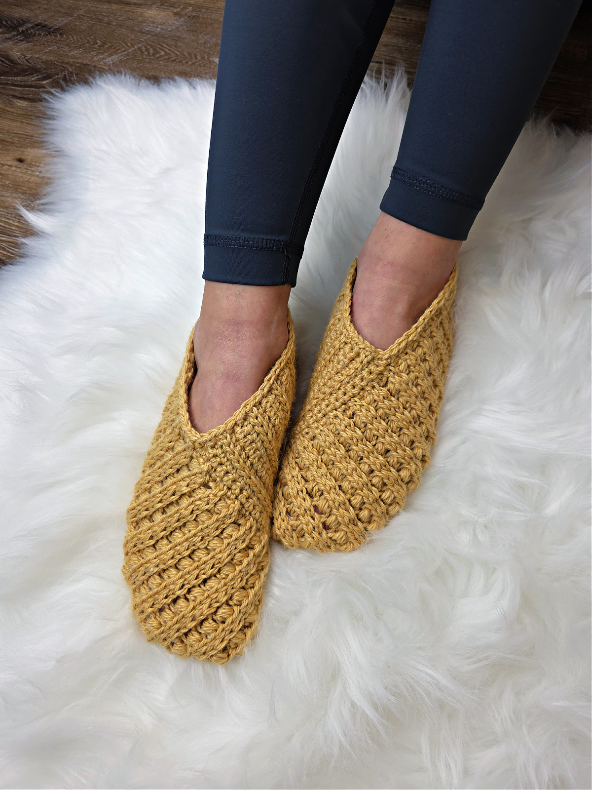 Model wearing mustard crochet slippers on feet and blue leggings.