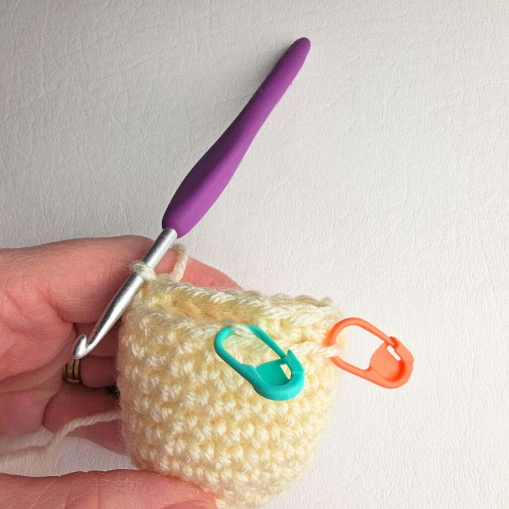 Small ivory crochet head for an ornament and a purple crochet hook and stitch markers.