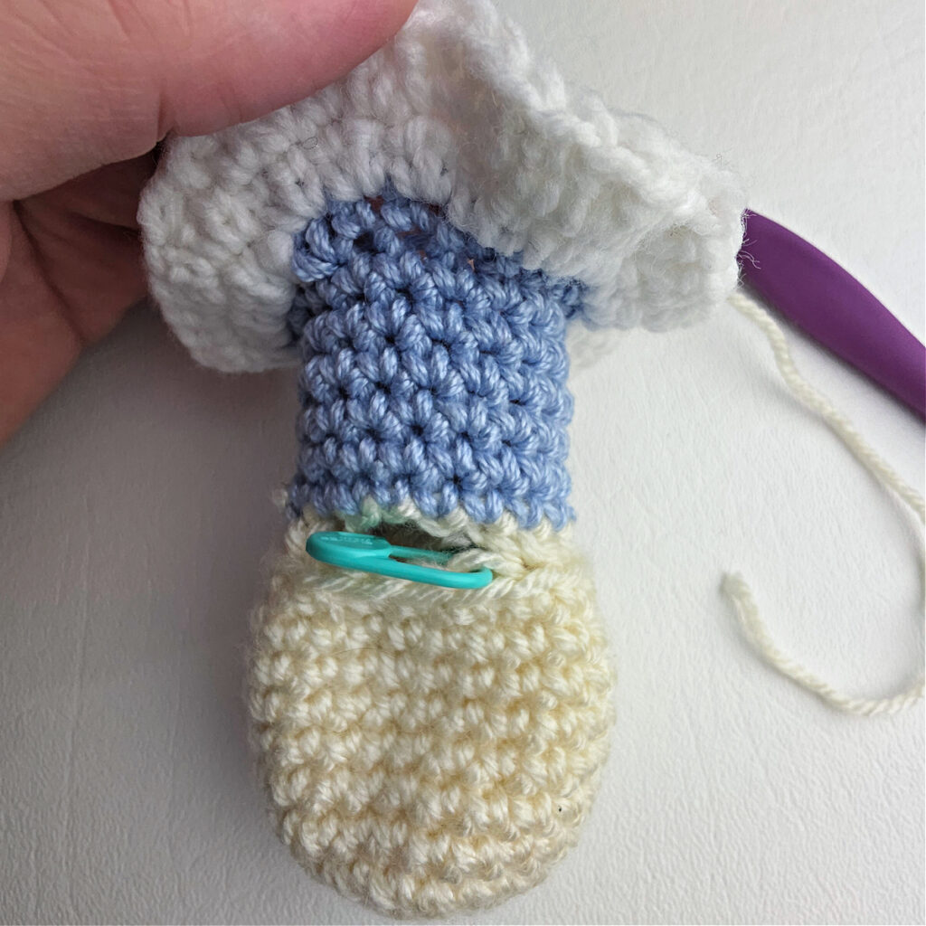 Crochet body upside down with a blue stitch marker showing where to join yarn for the arm.