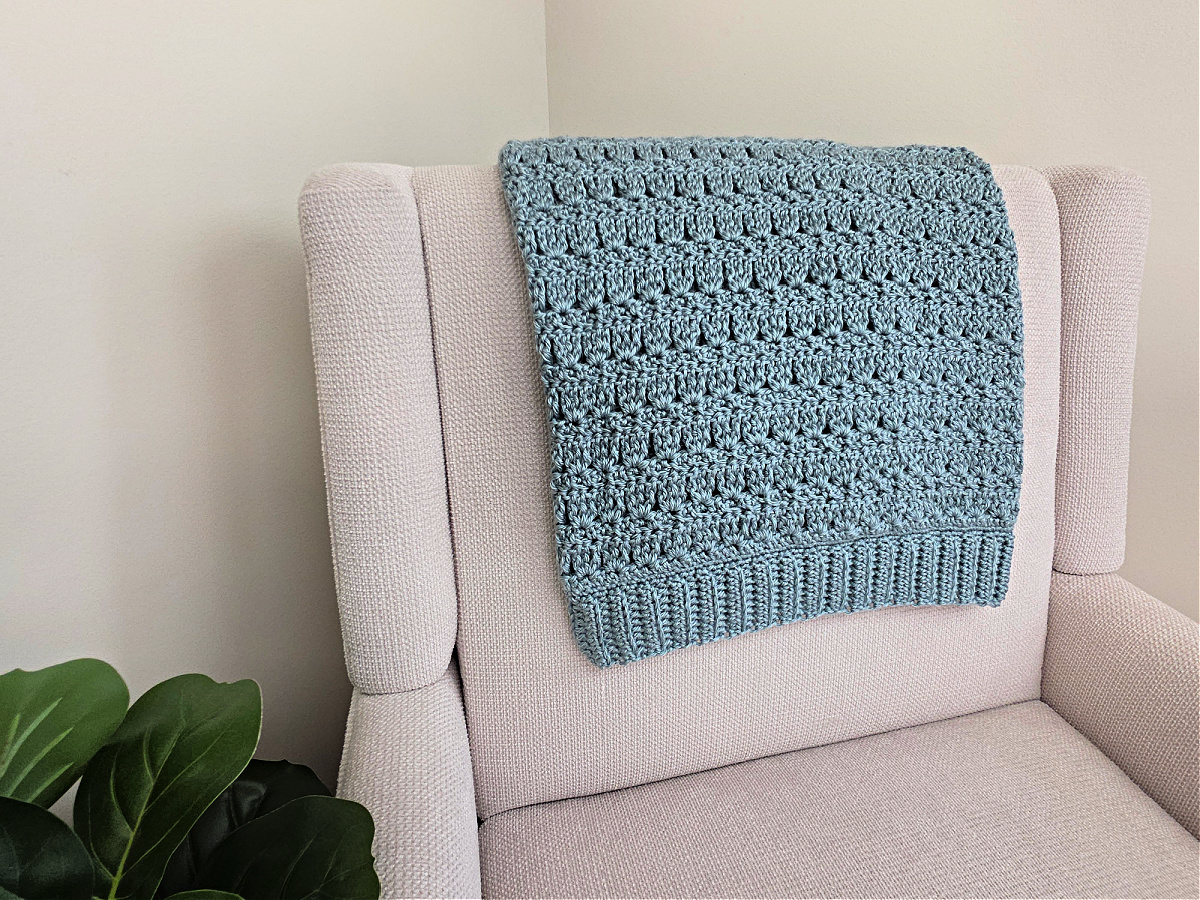 Blue crochet throw blanket on a white sofa with a plant next to it.