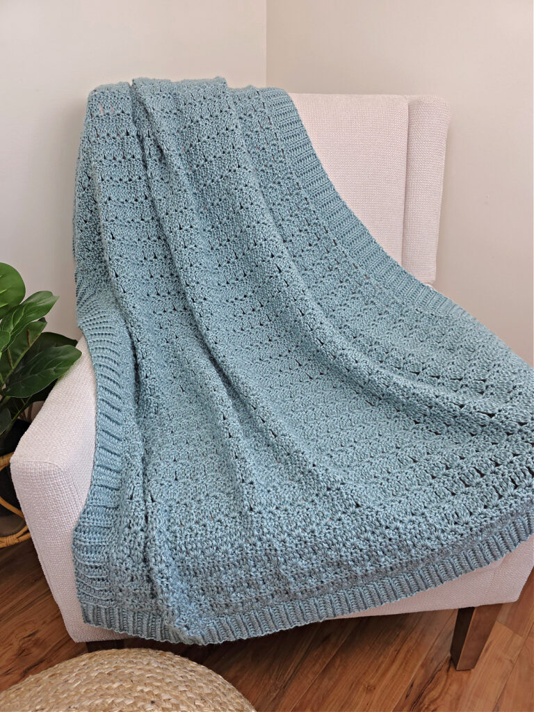 Blue crochet throw blanket on a white sofa with a plant next to it.