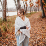 A woman standing on a path of fallen leaves wearing a grey crochet triangular shawl.