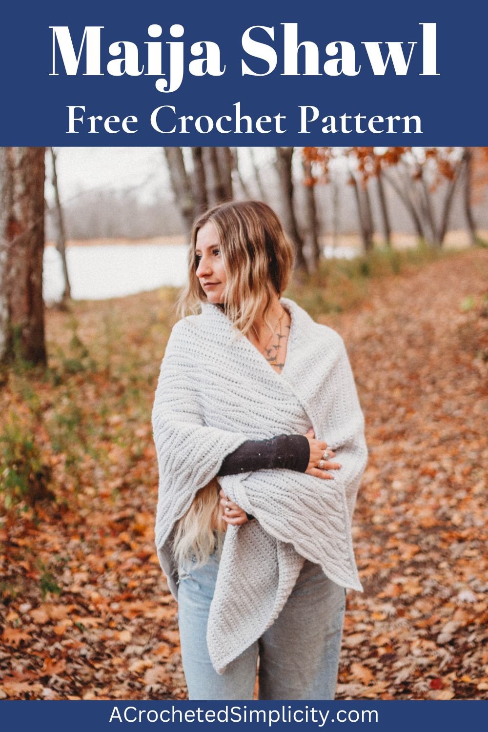 A woman standing on a path of fallen leaves wearing a grey crochet triangular shawl.
