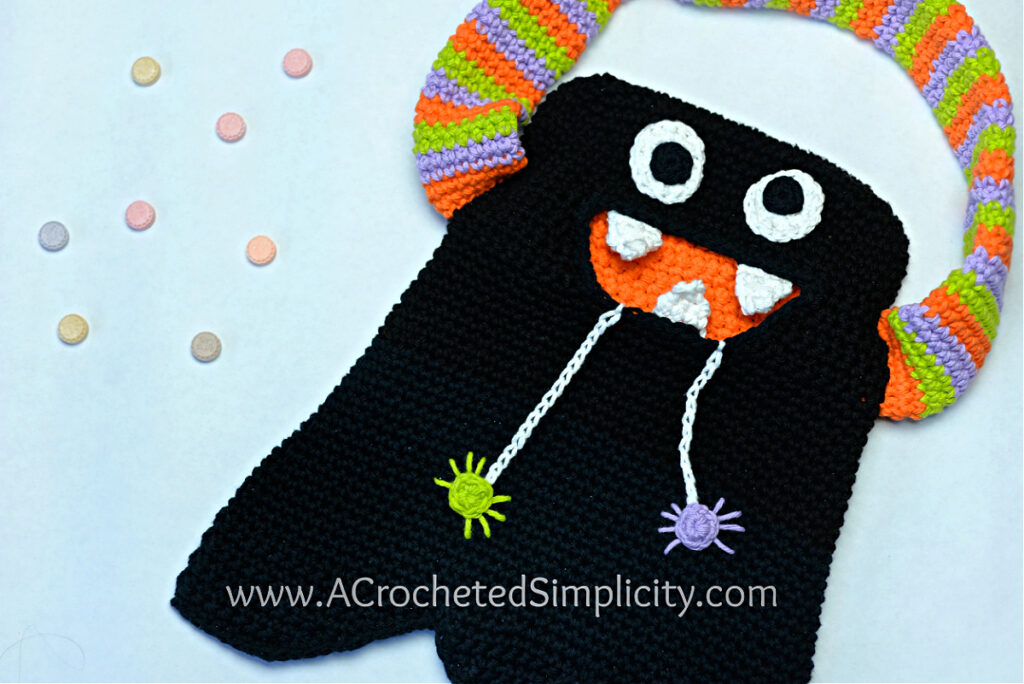 A black monster bag with a colorful handle and a wide toothy grin and two crocheted spiders.