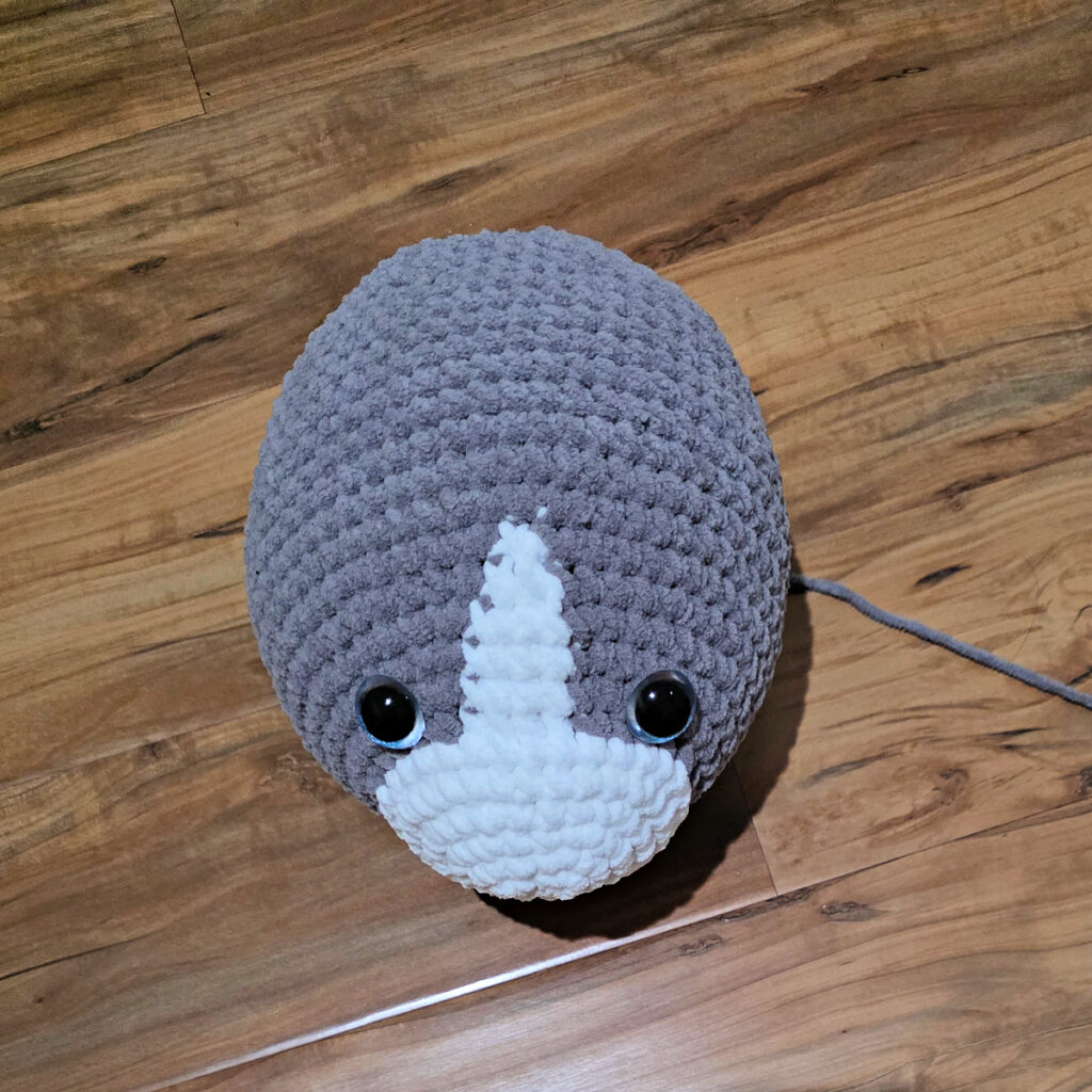 In process of making a crochet cat laying against a wooden floor.