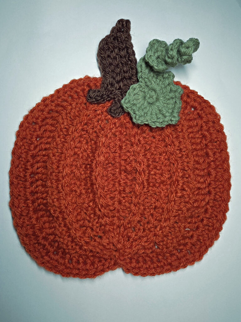 An orange crochet pumpkin with green leaves and brown stem.