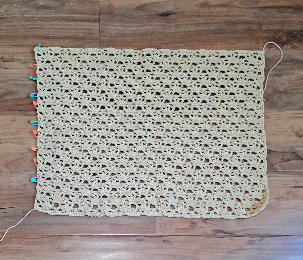 A beige colored cropped crochet cardigan in progress.