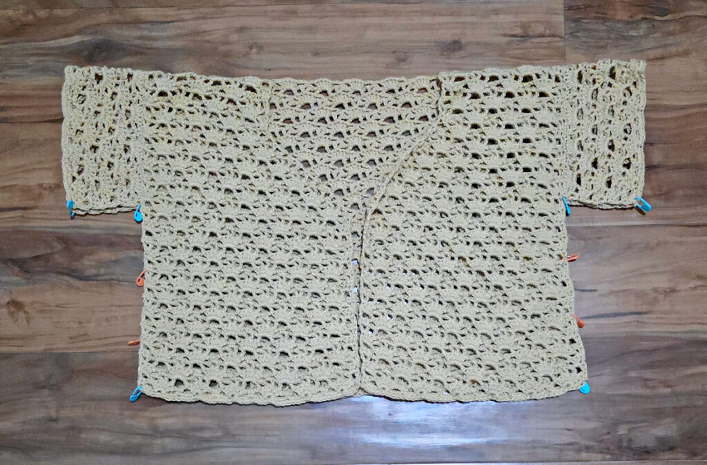 A beige colored cropped crochet cardigan in progress.