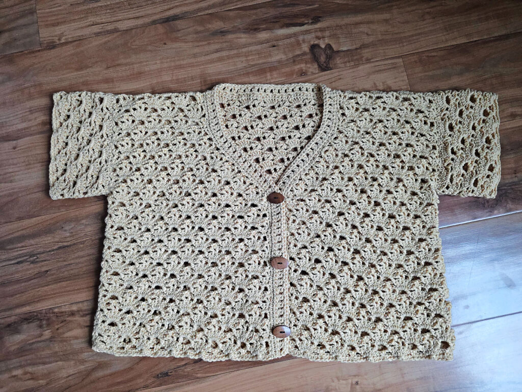 A beige colored cropped crochet cardigan against a wooden floor.
