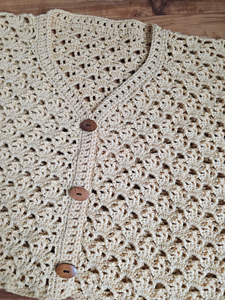 A beige colored cropped crochet cardigan against a wooden floor.