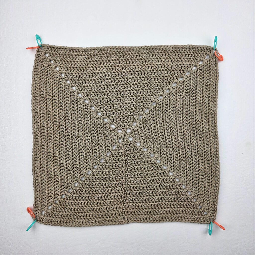 A large crochet square with stitch markers around the edge.