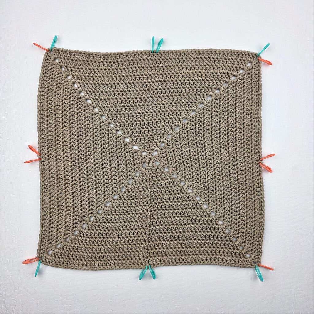 A large crochet square with stitch markers around the edge.
