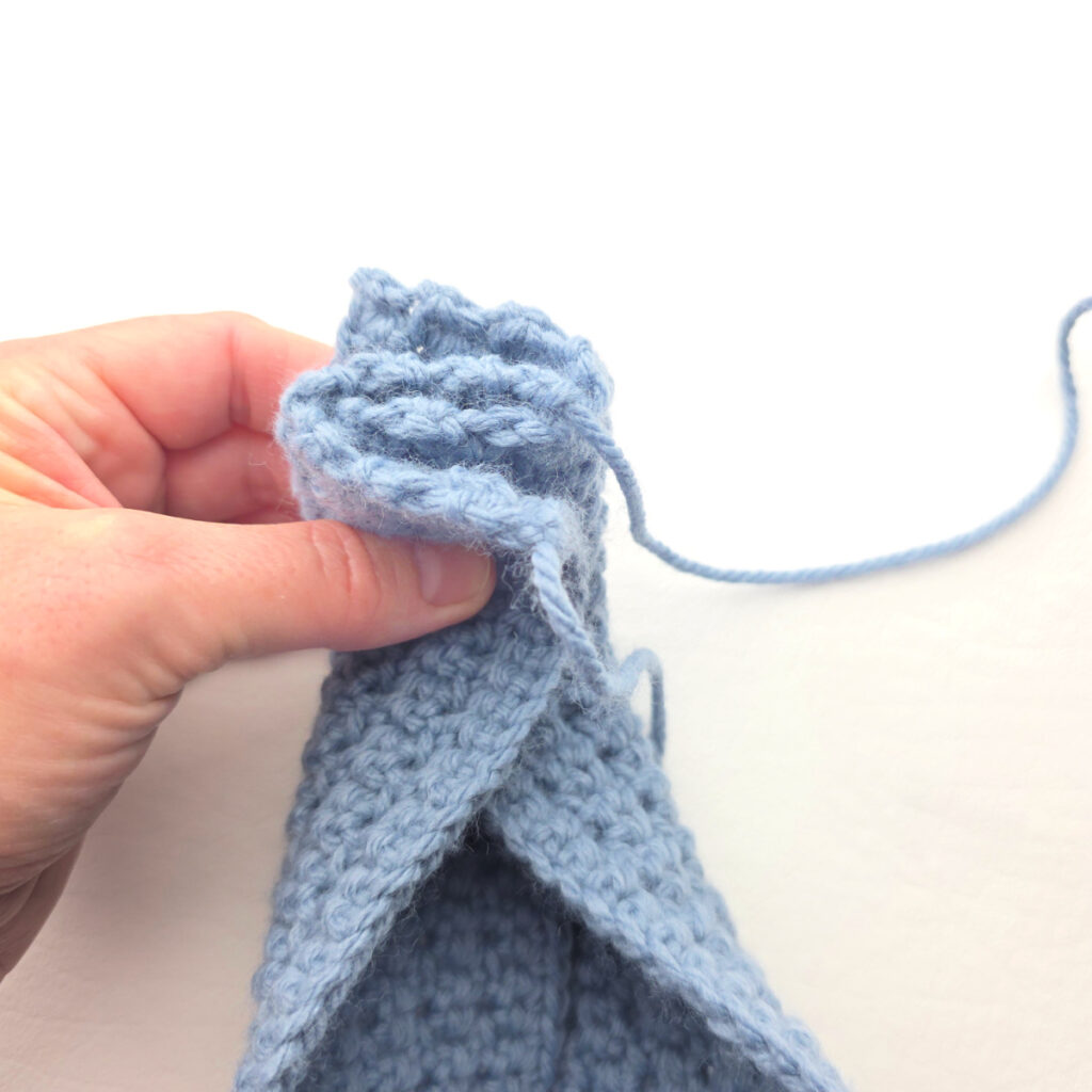 The ends of a handmade gray crochet ear warmer being stitched.