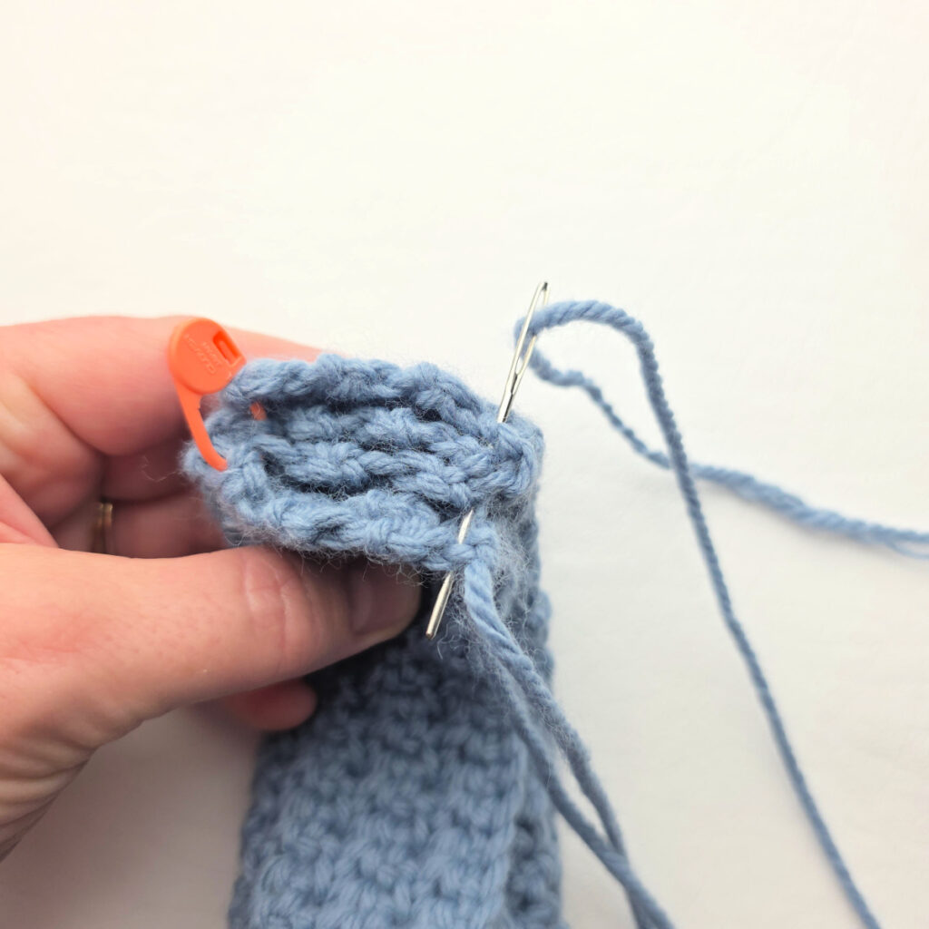 The ends of a handmade gray crochet ear warmer being stitched.