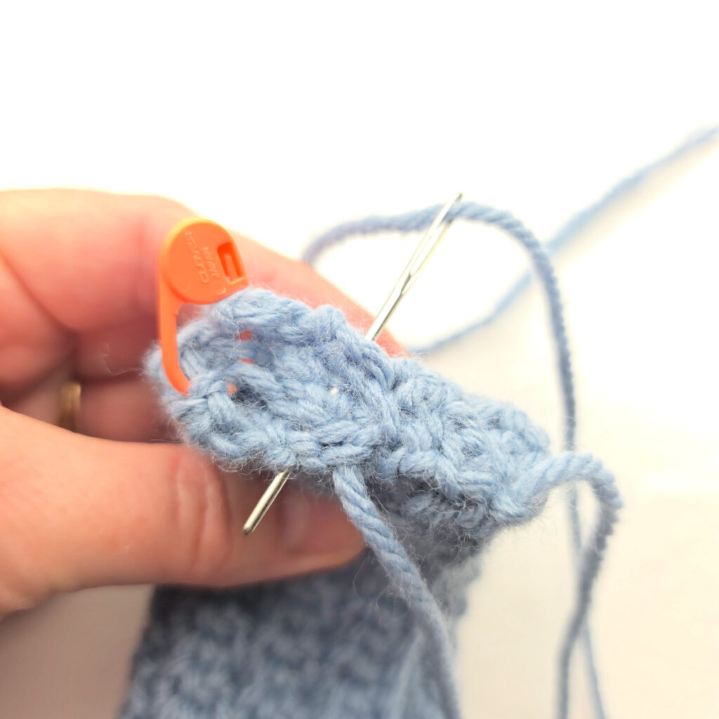 The ends of a handmade gray crochet ear warmer being stitched.