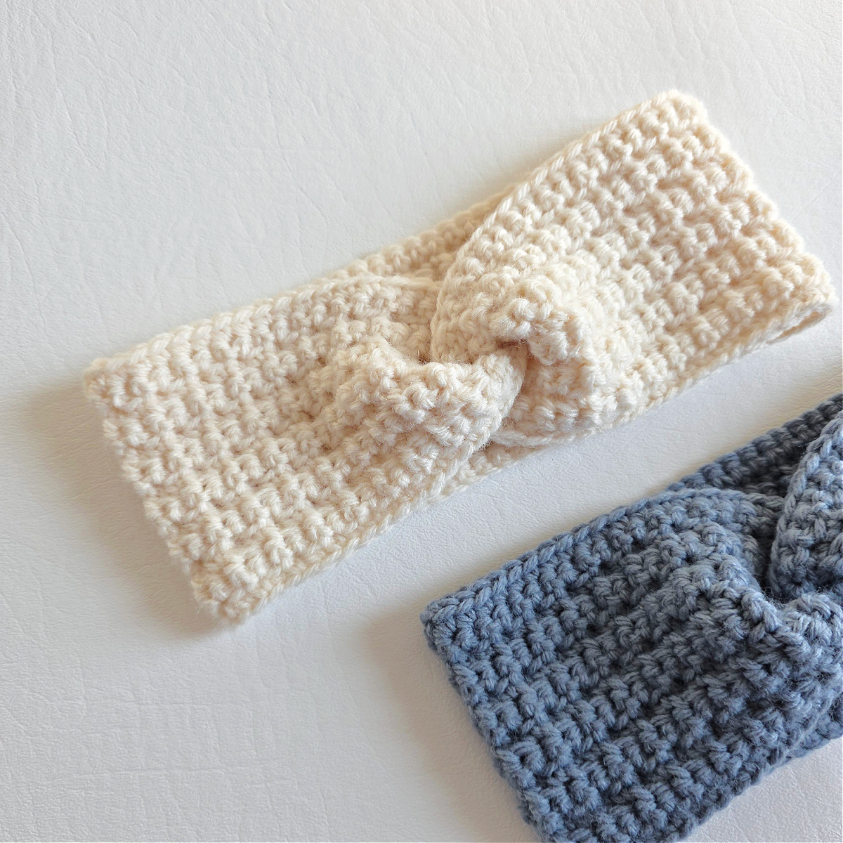 A gray crochet ear warmer and white crochet ear warmer against a white background.