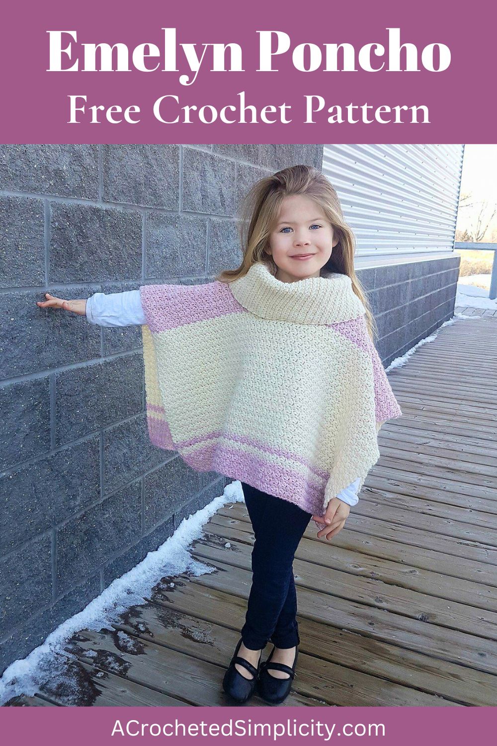 A child wearing a cream and pink colored poncho and black bottoms standing with her hand on the wall.