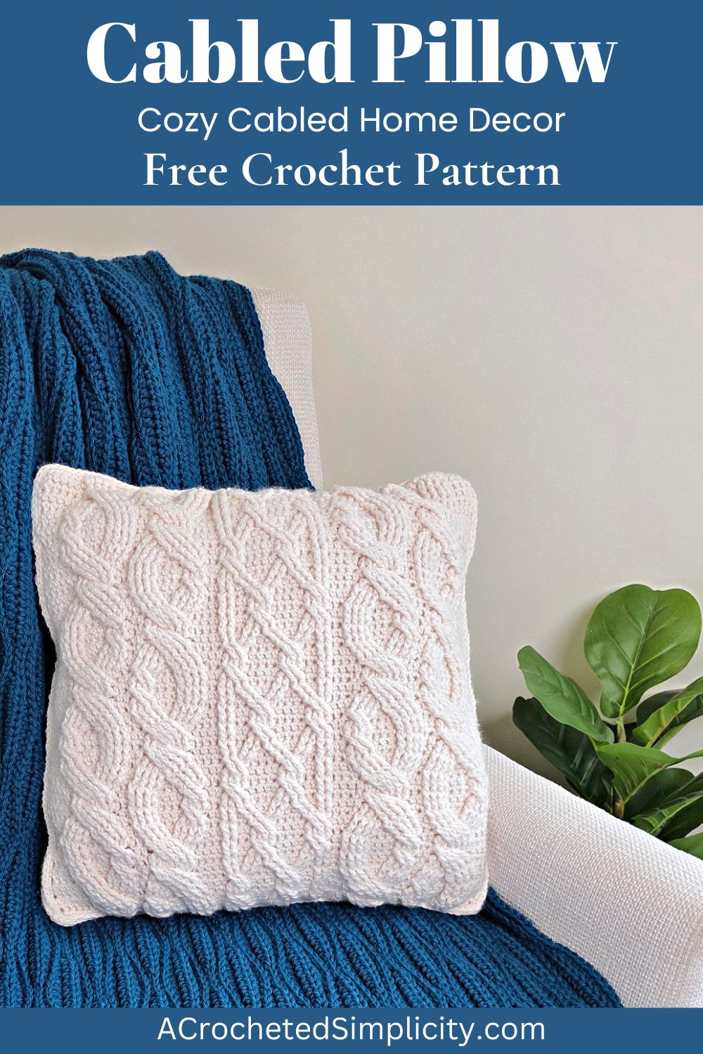 White cabled crochet pillow on a sofa with a blue crochet blanket behind it and a plant next to it.