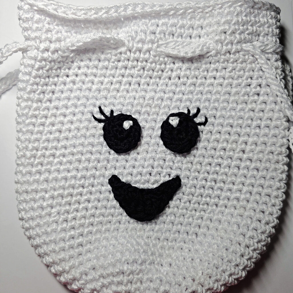 A crochet ghost treat bag with a smiley face.