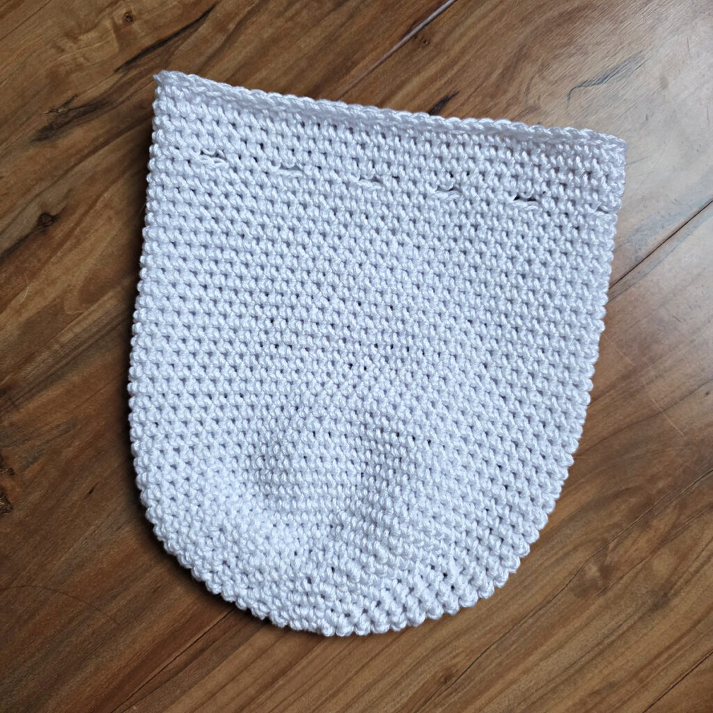 The body of a crochet ghost treat bag on a wooden floor.