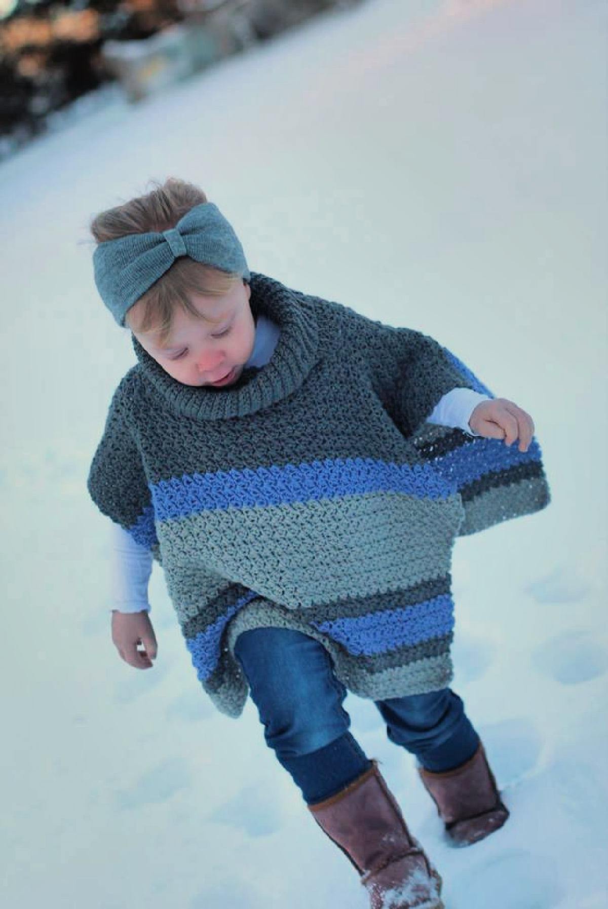 A child wearing a gray and blue colored poncho playing in the snow.